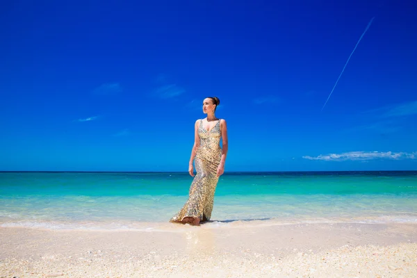 Young beautiful girl in gold dress on the beach of a tropical is — Stock Photo, Image