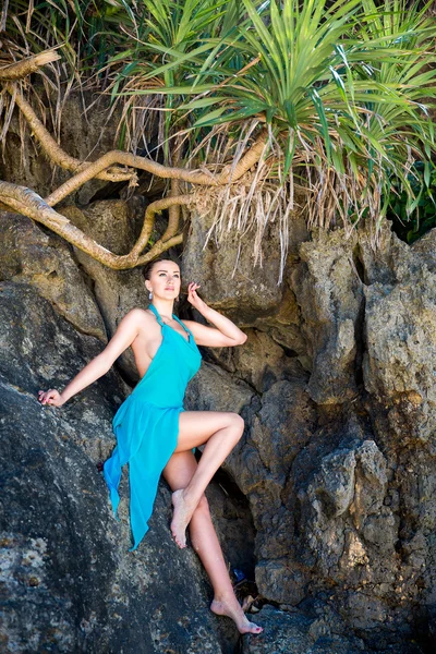 Young beautiful girl in blue dress on the rock of a tropical isl — Stock Photo, Image