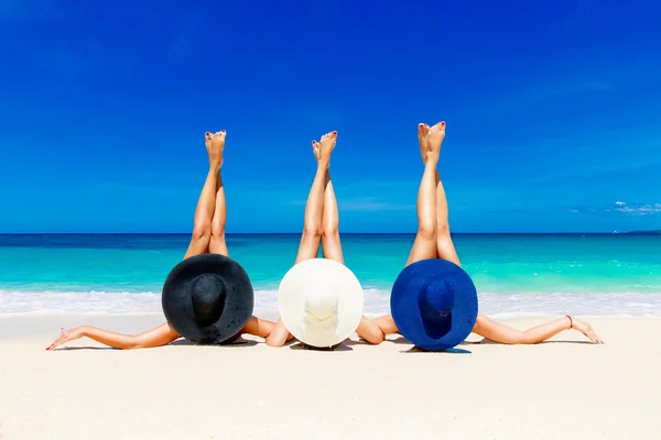 Tre giovani donne in cappelli di paglia sdraiate su una spiaggia tropicale, stret — Foto Stock