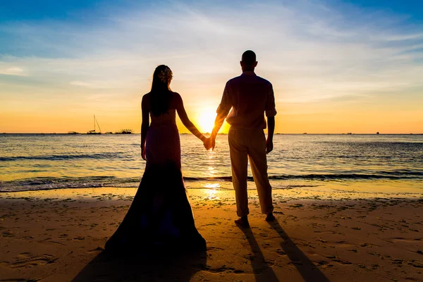 The bride and groom are kept hands on a tropical beach . Silhoue — Stock Photo, Image