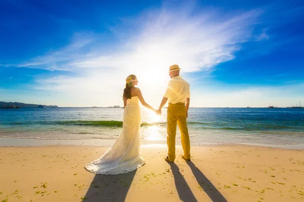 Bride and groom on a tropical beach with the sunset in the backg — Stock Photo, Image