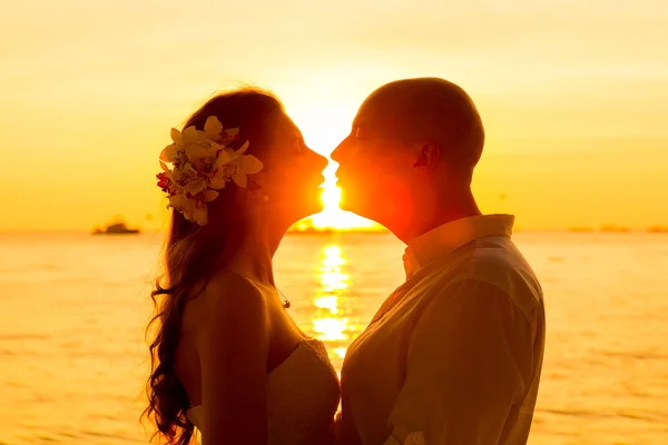 Nevěsta a ženich líbat na tropické pláži při západu slunce — Stock fotografie