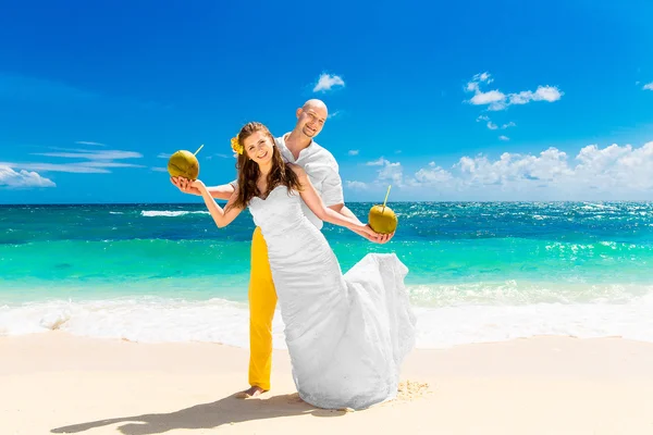 Glückliche Braut und Bräutigam trinken Kokoswasser an einem tropischen Strand. w — Stockfoto