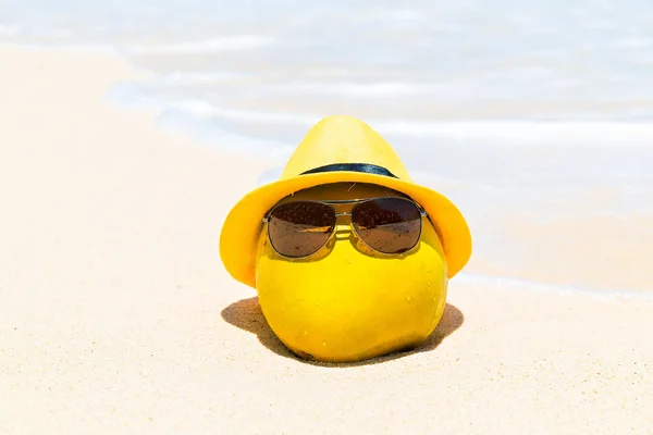 Funny coco en gafas de sol y sombrero amarillo se encuentra en un tropi arenoso —  Fotos de Stock
