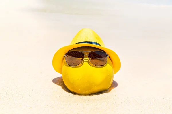 Funny coconut in sunglasses and yellow hat lies on a sandy tropi — Stock Photo, Image