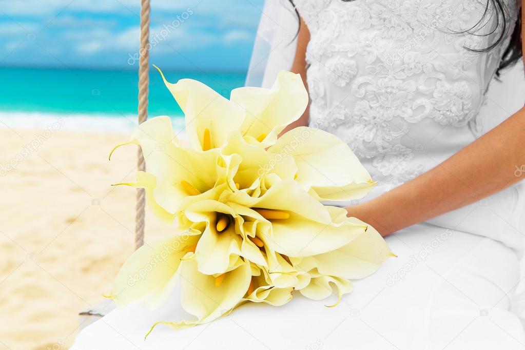 Wedding bouquet lying on the lap of the bride on a tropical beac