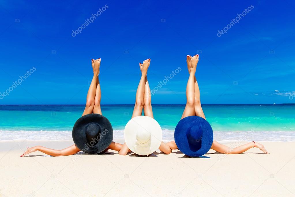 Three young women in straw hats lying on a tropical beach, stret