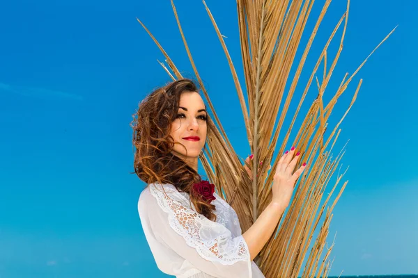 Happy young brunette in white dress sianding with palm leaves on — Stock Photo, Image