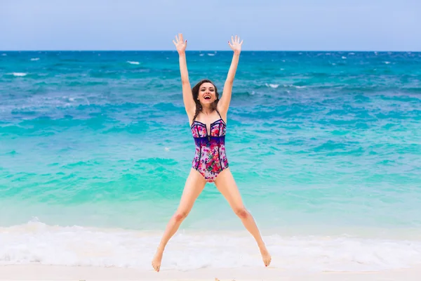 Giovane bruna felice in costume da bagno su una spiaggia tropicale. Mare blu — Foto Stock