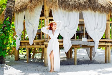 Young beautiful girl in white dress stands next a bamboo hut on 