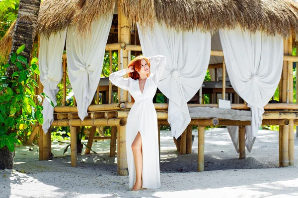 Joven hermosa chica en vestido blanco se encuentra junto a una cabaña de bambú en — Foto de Stock