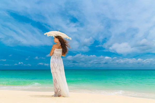 Schöne junge Frau im weißen Kleid mit Regenschirm auf einem tropischen — Stockfoto