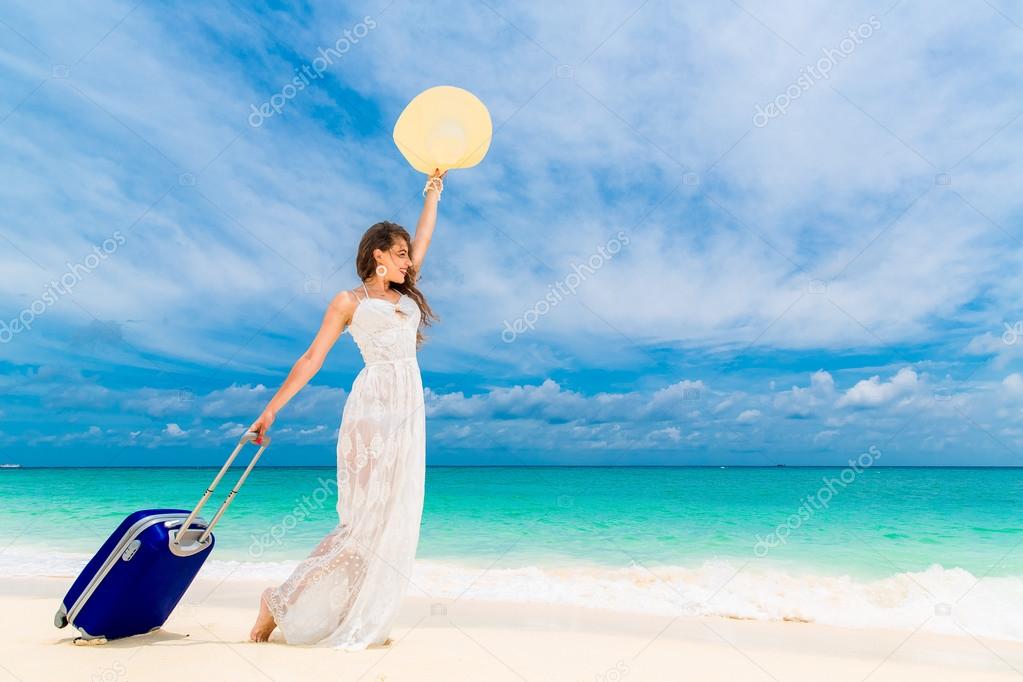 Beautiful young woman in white dress and straw hat with a suitca
