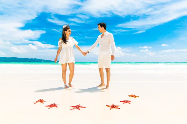 Novia y novio en la orilla de la playa tropical con estrellas de mar rojas en el — Foto de Stock