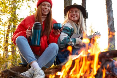 Bir grup genç, doğada şenlik ateşinin yanında dinleniyor.