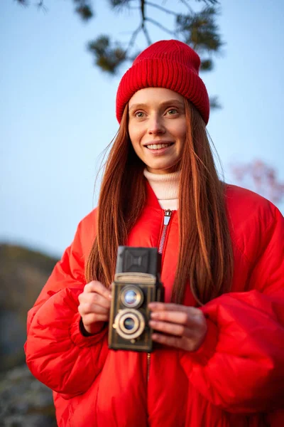 Νεαρή κοκκινομάλλα γυναίκα λήψη φωτογραφιών το φθινόπωρο δάσος χρησιμοποιώντας vintage κάμερα — Φωτογραφία Αρχείου