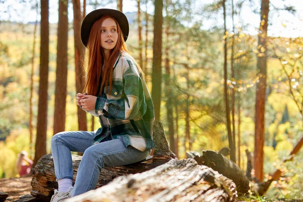 Ruiva viajantes mulher senta-se na árvore velha, toco na floresta — Fotografia de Stock