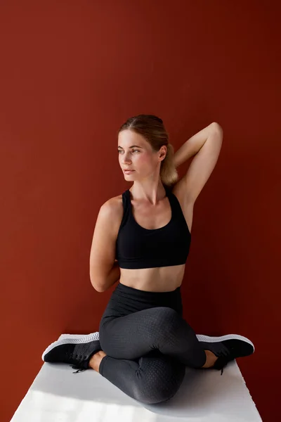 Atletik kadın bütün vücudunu esnetiyor ve tek başına kutunun üzerinde oturuyor. — Stok fotoğraf