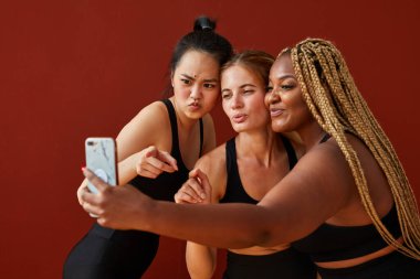 Farklı ırk ve beden ölçülerinde üç farklı etnik kadın model izole edilmiş kamerada selfie çekiyor.