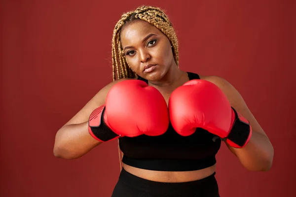 赤の背景に赤のボクシングミットを持つアフリカのオーバーサイズ女性 — ストック写真