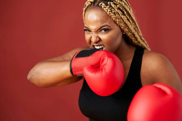 african oversize woman with red boxing mitts isolated on red background