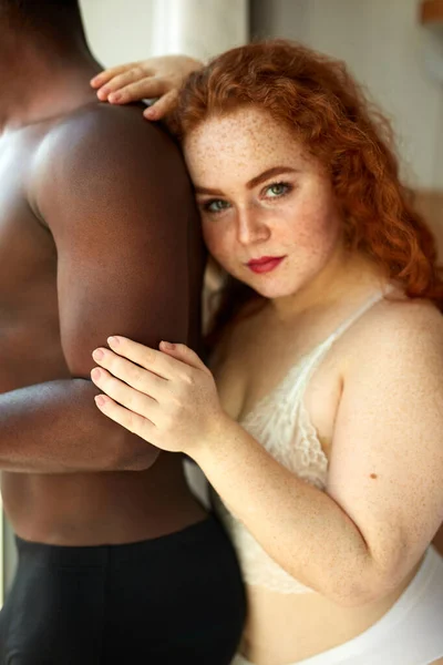 Приваблива товста жінка з імбирним волоссям обіймає чорного хлопця ззаду — стокове фото