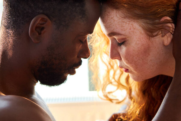 любящая любящая обнаженная межрасовая пара в постели, собирается поцеловаться