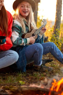 Bir grup genç, doğada şenlik ateşinin yanında dinleniyor.