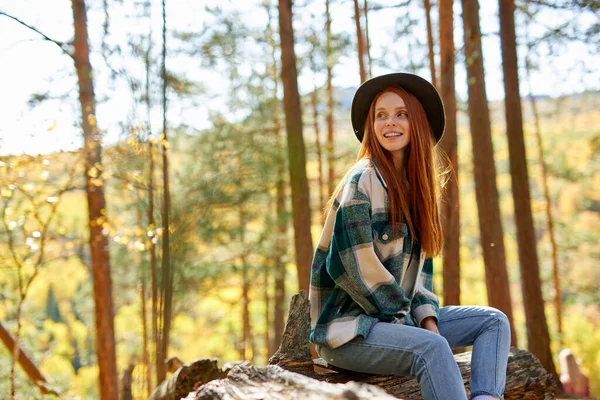 Redhead travellers woman sits on old tree, stump in the forest — Stock Photo, Image