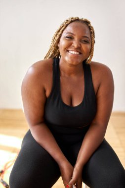 Tombul, artı Afrikalı Afro-Amerikan kadın spor kıyafetleri içinde kameraya bakarak oturuyor.