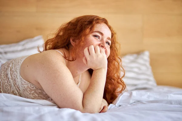 Dulce regordeta mujer con pelo rojo rizado en la cama en casa — Foto de Stock