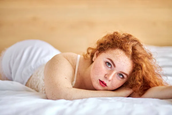 Encantadora joven con el pelo rojo natural posando en la cámara, acostado en la cama —  Fotos de Stock