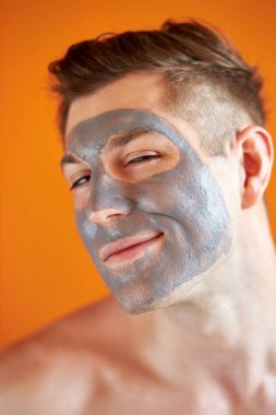 Yakışıklı genç adam, izole edilmiş sarı arka planda kameraya poz vererek spa tedavisi görüyor.