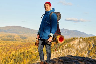 Sırt çantalı genç adam dağın zirvesinde duruyor.