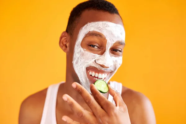 Portré őrült fekete férfi eszik uborka, miközben arc szépség maszk — Stock Fotó