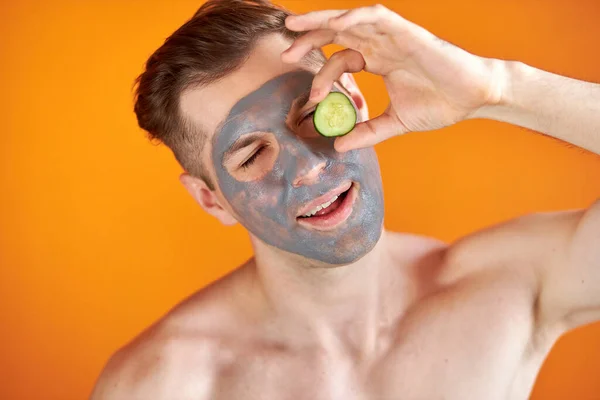 Postive férfi alkalmazni arc maszk uborka, kifejezni pozitív érzelmek — Stock Fotó
