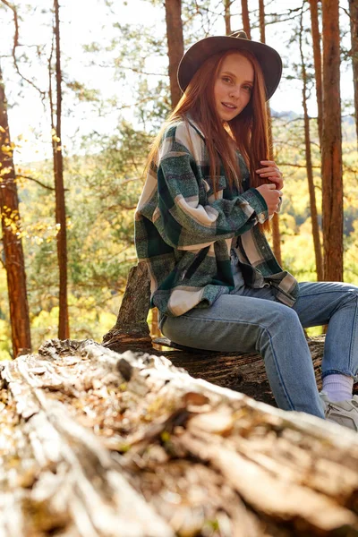 Roodharige reiziger vrouw zit op oude boom, stomp in het bos — Stockfoto