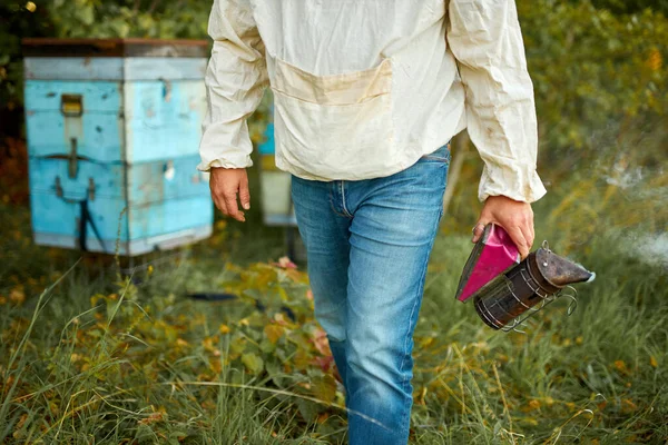 Granjero caucásico cuidando sus colmenas de abejas con fumador de abejas en su granja privada con cajas de abejas caseras —  Fotos de Stock