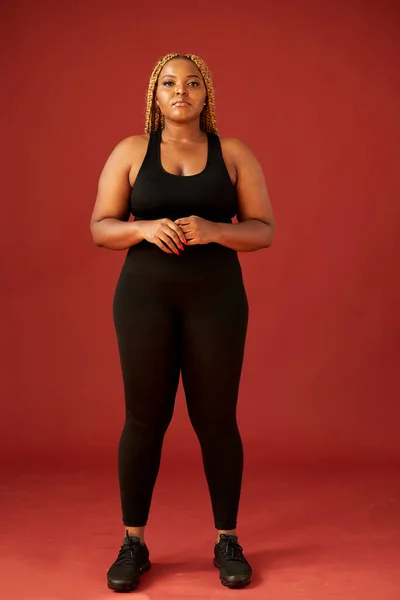 confident fat african woman in black sportswear isolated on red background
