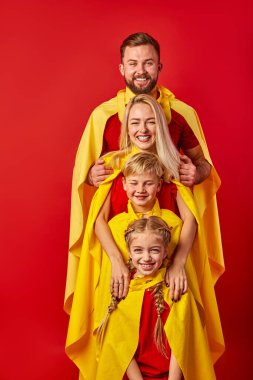 Dost canlısı beyaz bir aile üst üste, süper kahraman kostümleri giyiyorlar.