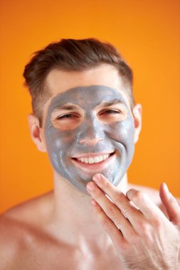 Yüzünde kozmetik kabuk maskesi olan genç ve yakışıklı bir adam.