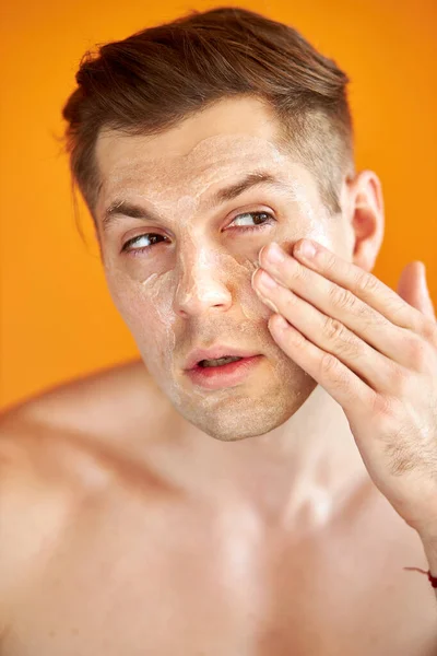 Νεαρός καυκάσιος άντρας εφαρμόζει ενυδατική κρέμα προσώπου για υγιές λαμπερό δέρμα, απομονωμένο — Φωτογραφία Αρχείου