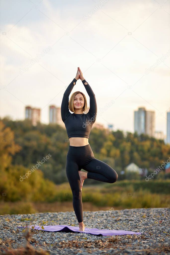 sporty fit caucasian woman doing hatha yoga asana vrikshasana tree pose outdoors