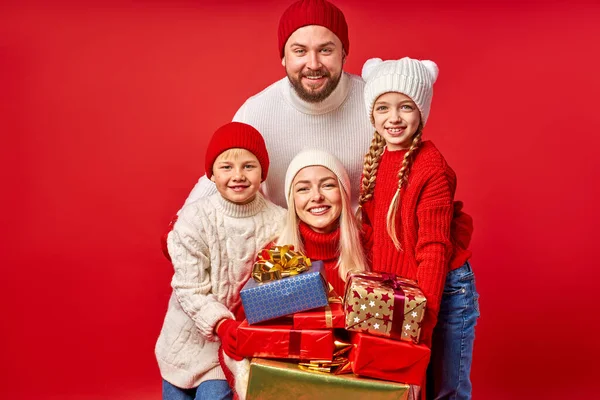 Счастливые родители и дети в зимней одежде держат подарки в руках изолированы на красный — стоковое фото