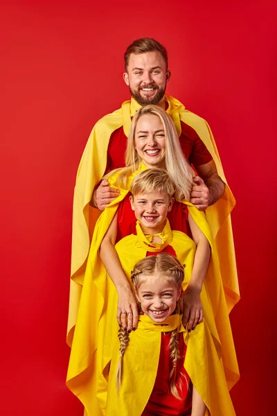 Super family in cloaks standing isolated on red background — Stock Photo, Image