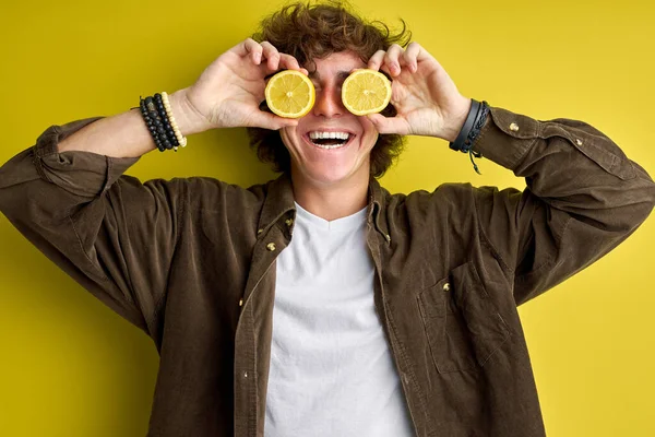 Stilig lockig tonåring pojke skrattar och gör narr med citron isolerad över grön bakgrund — Stockfoto