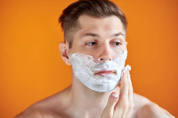 Hombre caucásico con espuma blanca en la cara, aislado sobre fondo naranja — Foto de Stock