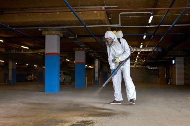 Koruyucu giysili temizlik işçisi. Basınçlı yıkama ya da dezenfektanla çalışıyor.