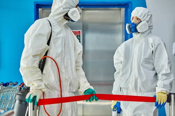 Hombres en traje de protección contra virus y máscara desinfectando edificios — Foto de Stock