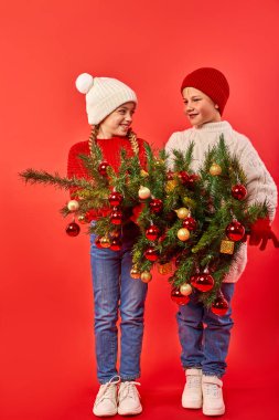 Kırmızı izole edilmiş arka planda küçük bir Noel ağacı olan mutlu çocukların stüdyo portresi